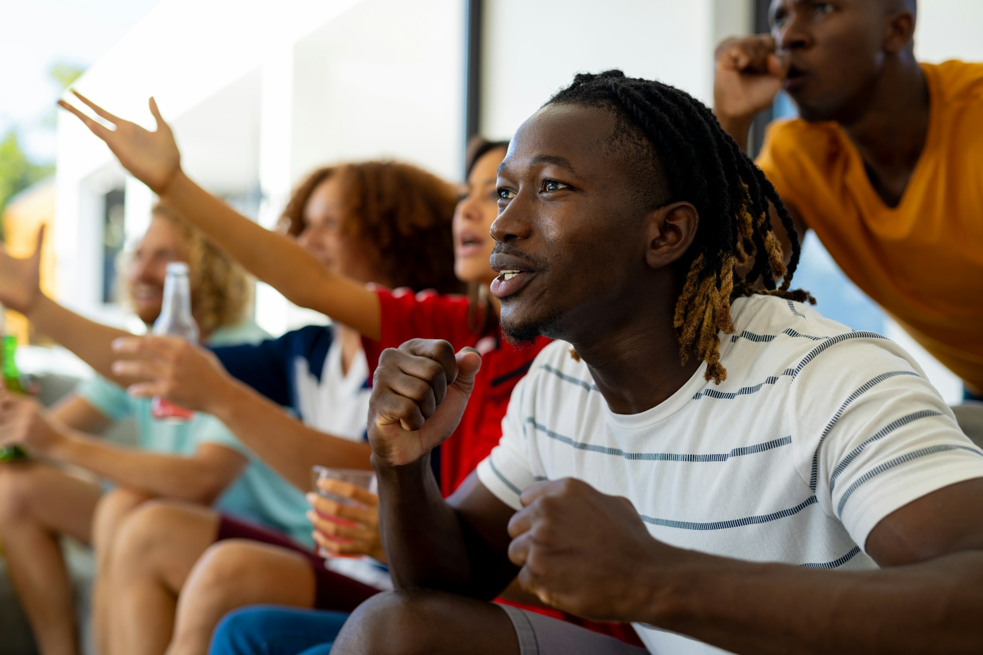 Group of excited diverse friends sitting on sofa, watching sport on tv